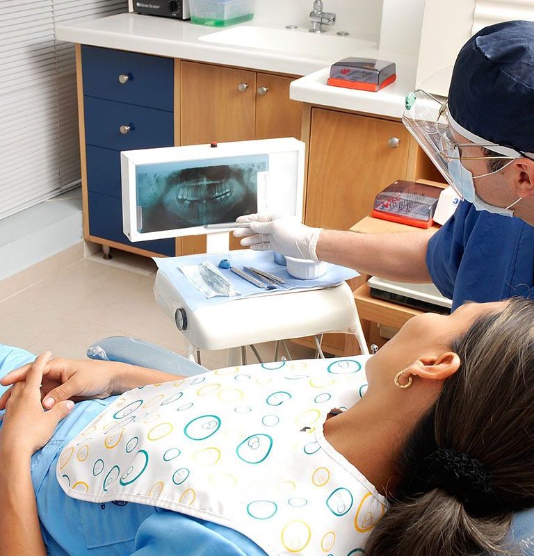Woman lies in exam chair and looks at xrays with healthcare provider.